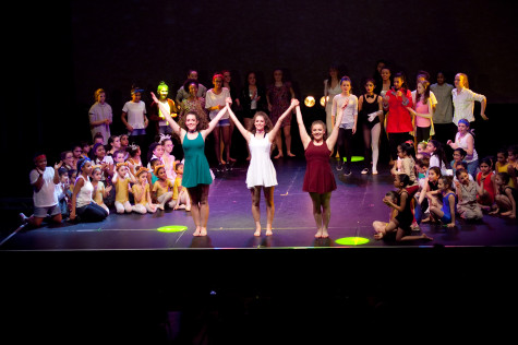 A picture of children of different ages on a stage, performing with three girls at the front of the stage.