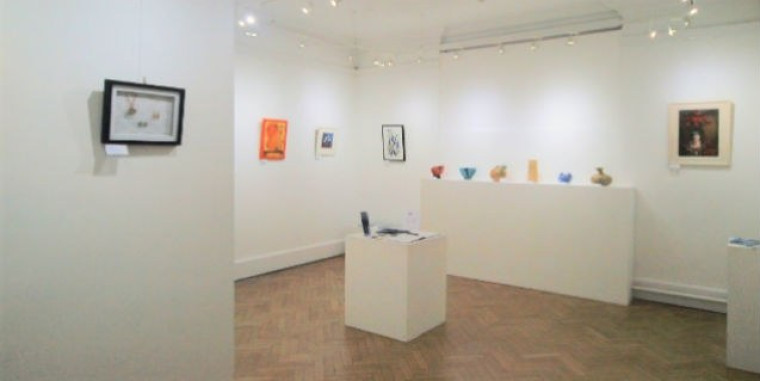 A picture of the art gallery, with paintings on the wall and a few stands with sculptures on them.