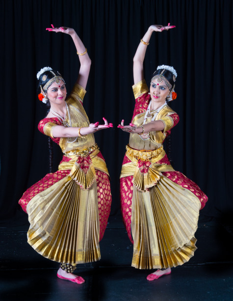 Two women are dressed up in Indian clothing, dancing.